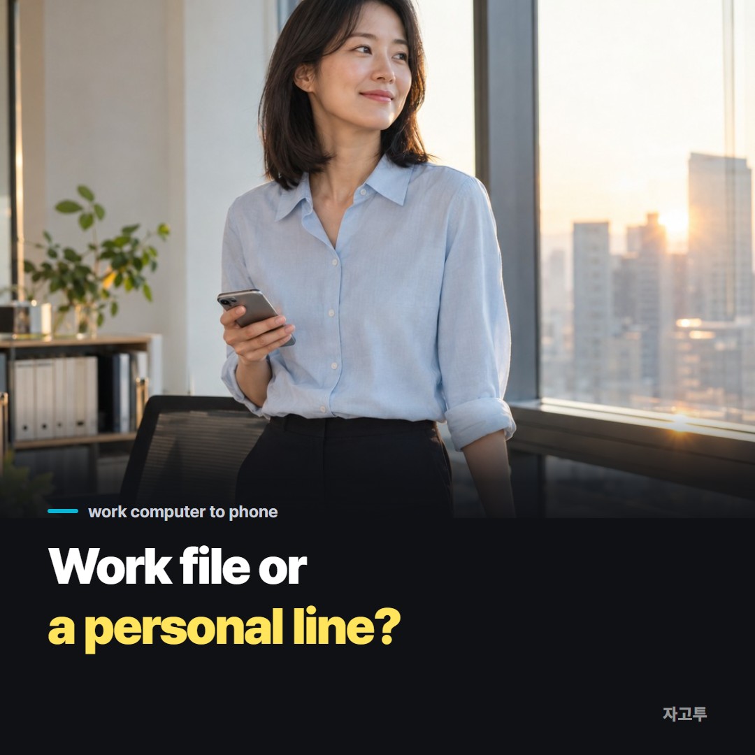 A person at an office desk holding a phone next to a work laptop at the end of the day